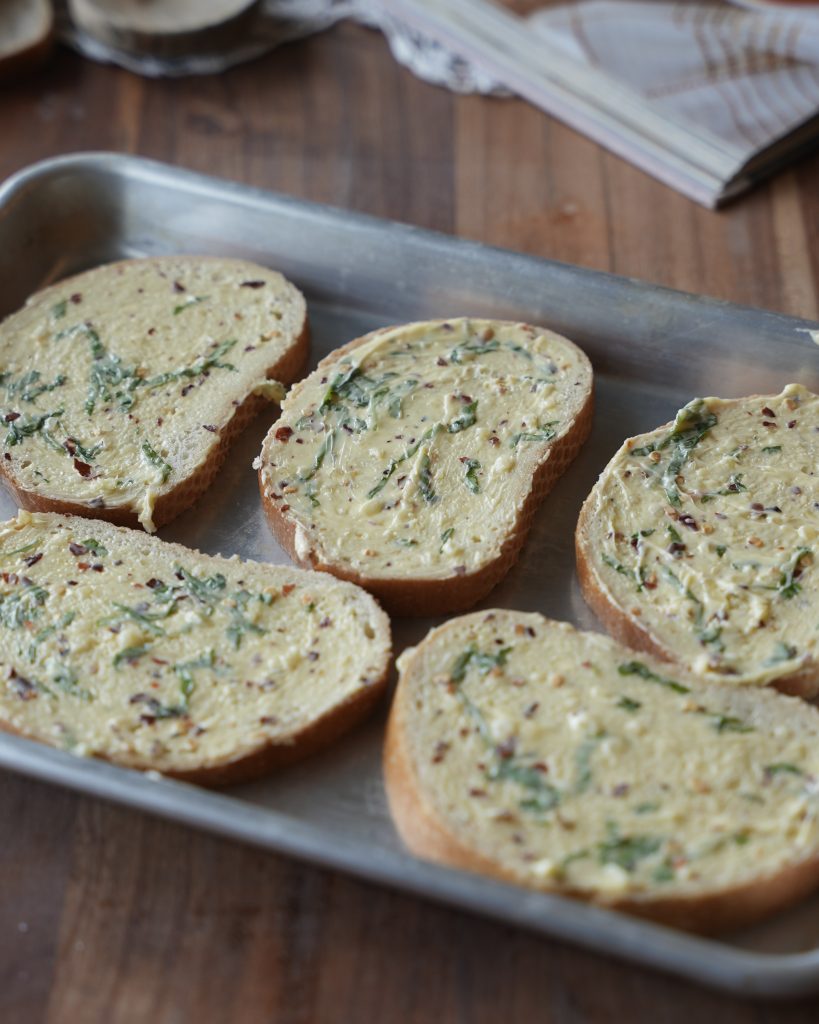 Bread slices spread with garlic basil butter on a sheet pan
