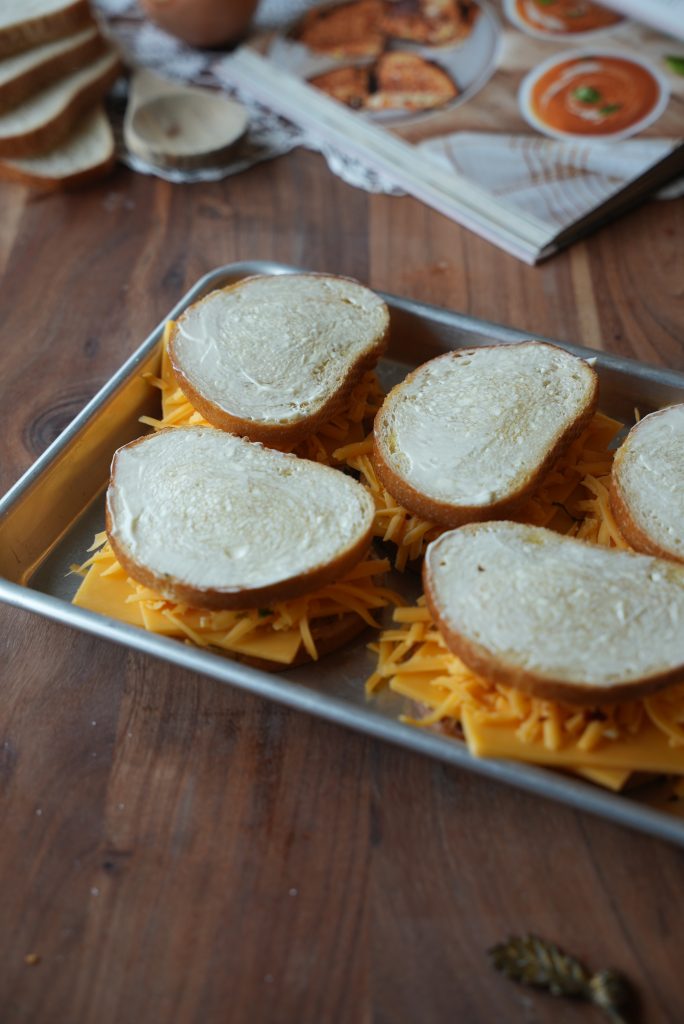 Sandwiches assembled with Cheddar and spread with mayo on a sheet pan