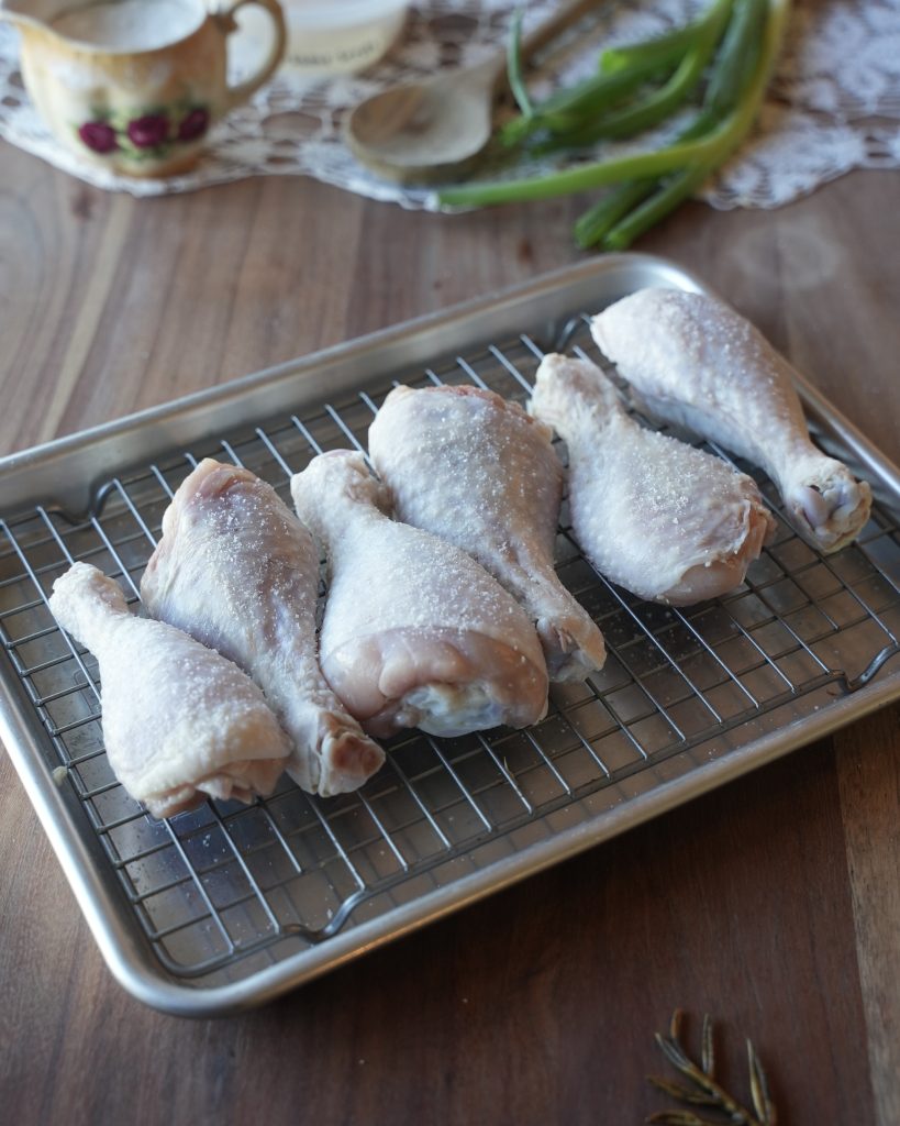 Salted chicken drumsticks drying on a wire rack